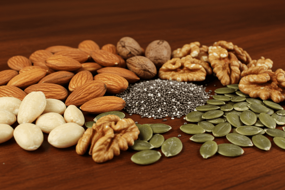 A variety of healthy nuts and seeds, including almonds, walnuts, chia seeds, and pumpkin seeds, on a wooden surface.